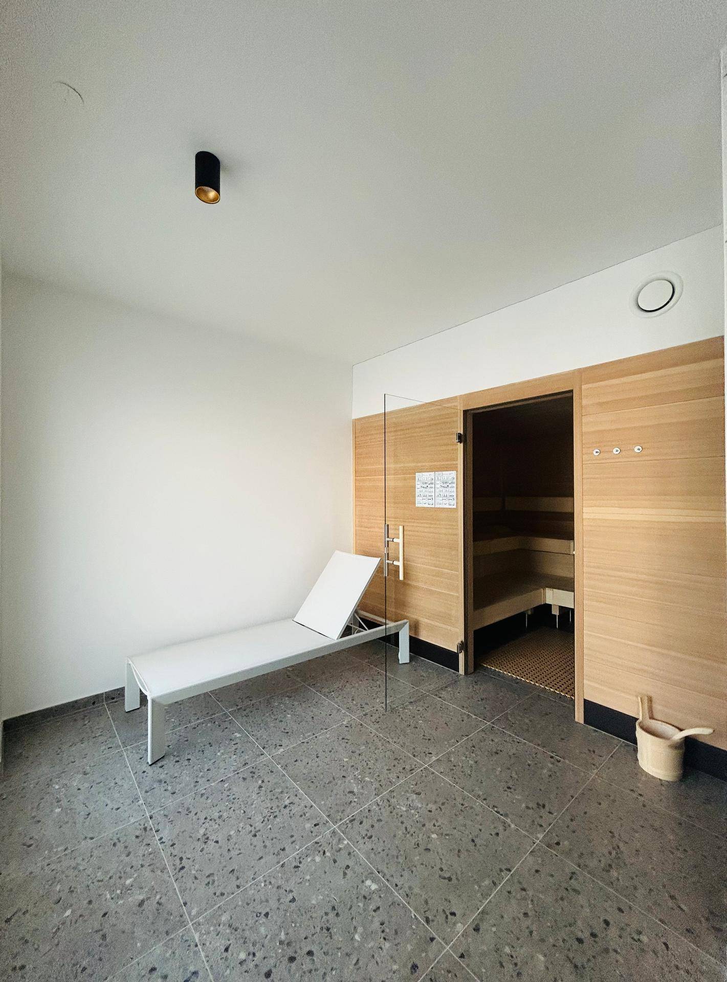 Entspannungsbereich mit Liege und Zugang zu einer modernen Holzsauna.
