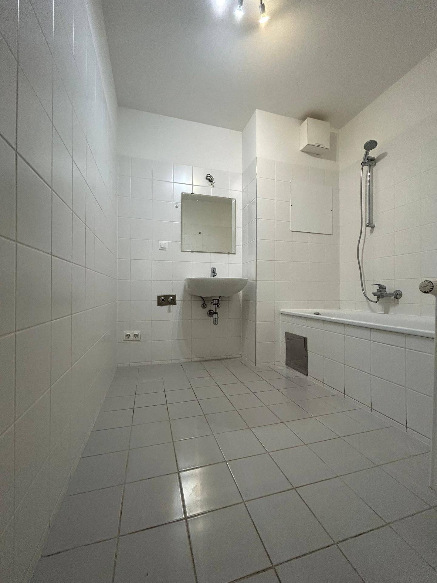 Gefliestes Badezimmer mit Badewanne, Duschkopf und Einzelwaschbecken.
