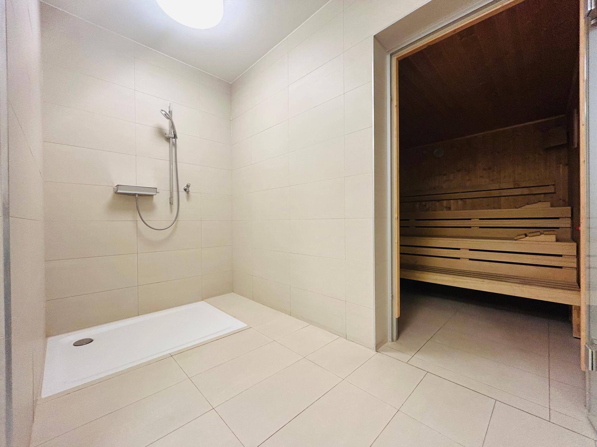 Duschbereich neben einer Holzsauna in einem modernen Wellnessbereich.