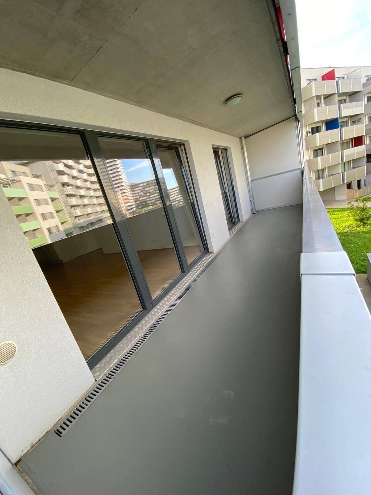 Geräumiger Balkon mit grauem Boden und Blick auf umliegende Gebäude.
