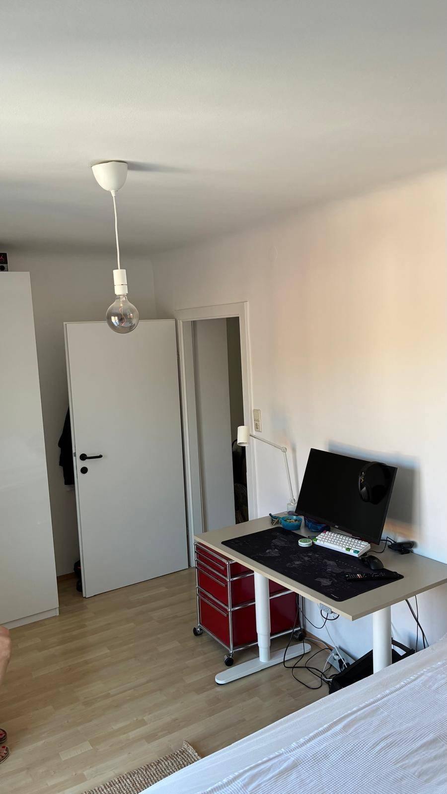 Helles Schlafzimmer mit Holzboden, Schreibtisch und einfacher Einrichtung.