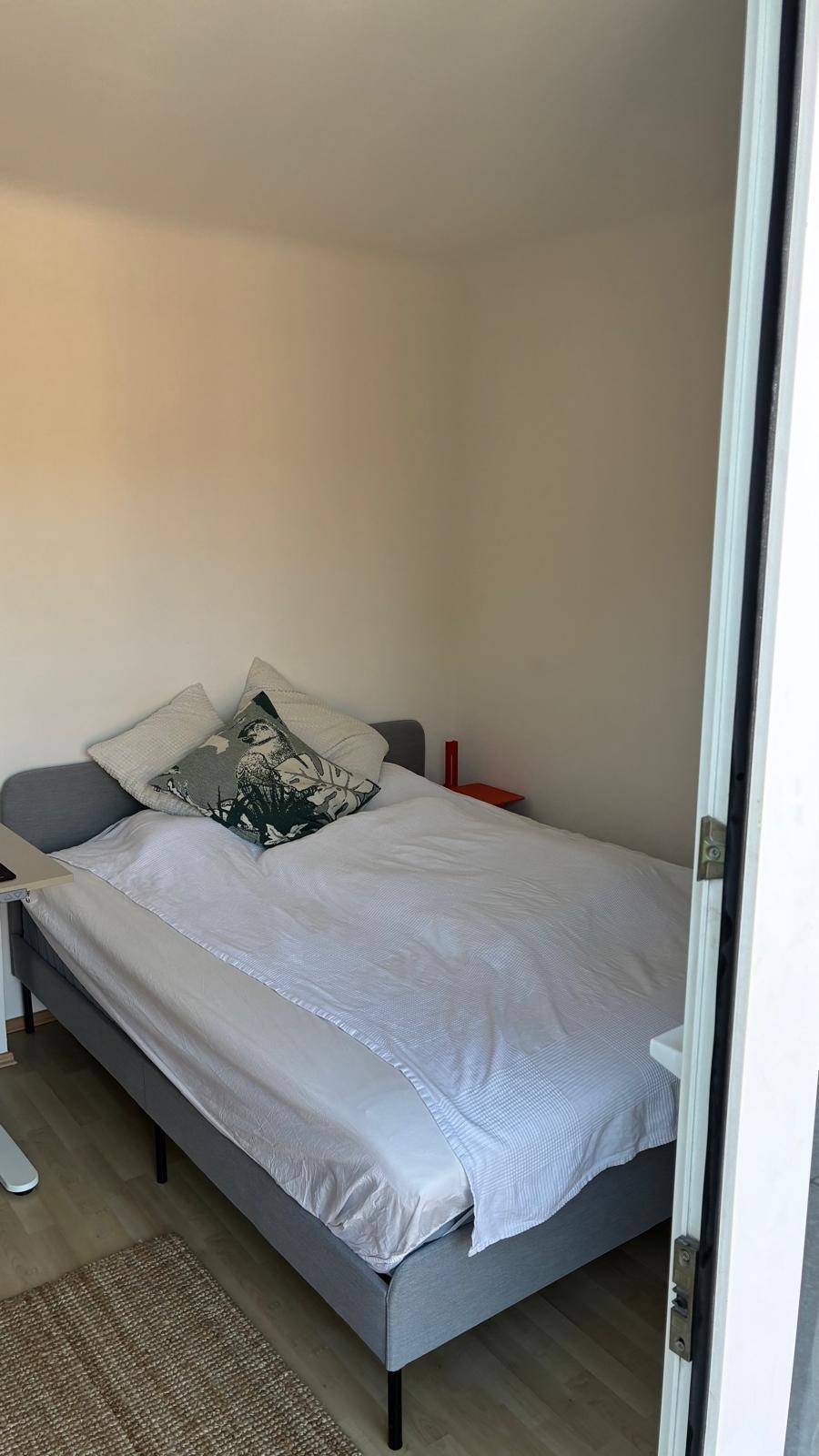 Gemütliches Schlafzimmer mit Doppelbett und hellem Holzboden, durch eine Tür sichtbar.