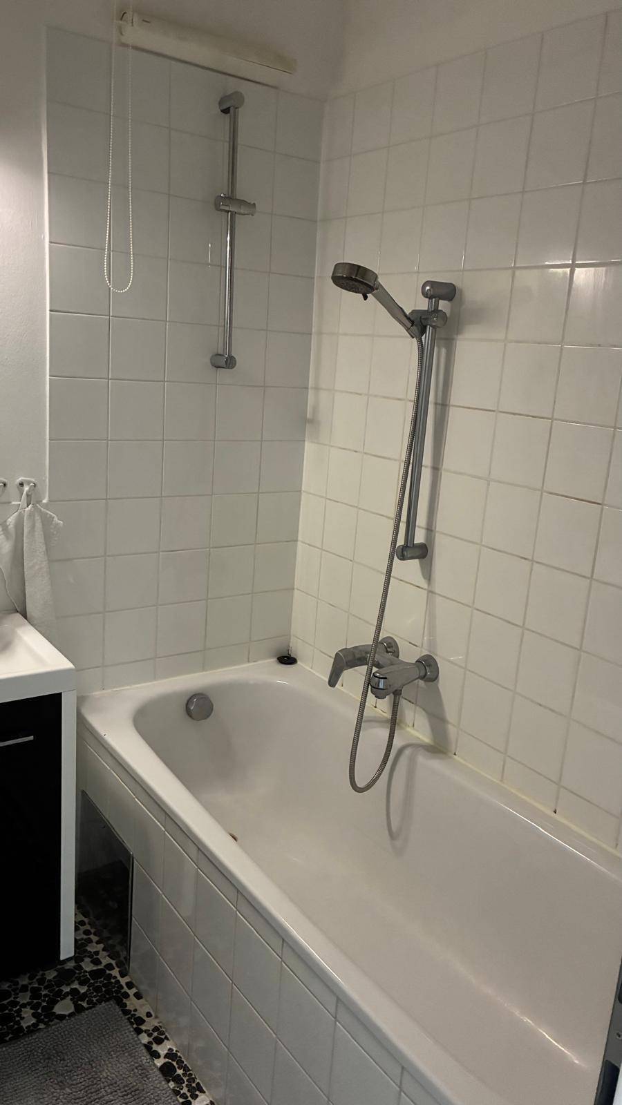 Badezimmer mit Badewanne und weißen Fliesen, ausgestattet mit einer Duscharmatur.
