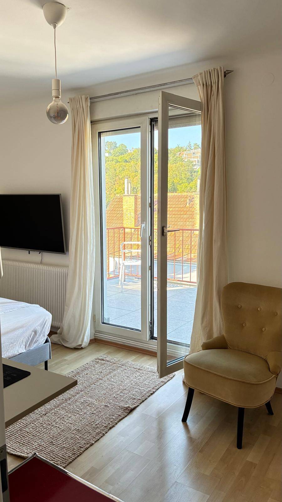Schlafzimmer mit Zugang zur Terrasse, Holzboden und einem gemütlichen Sessel.
