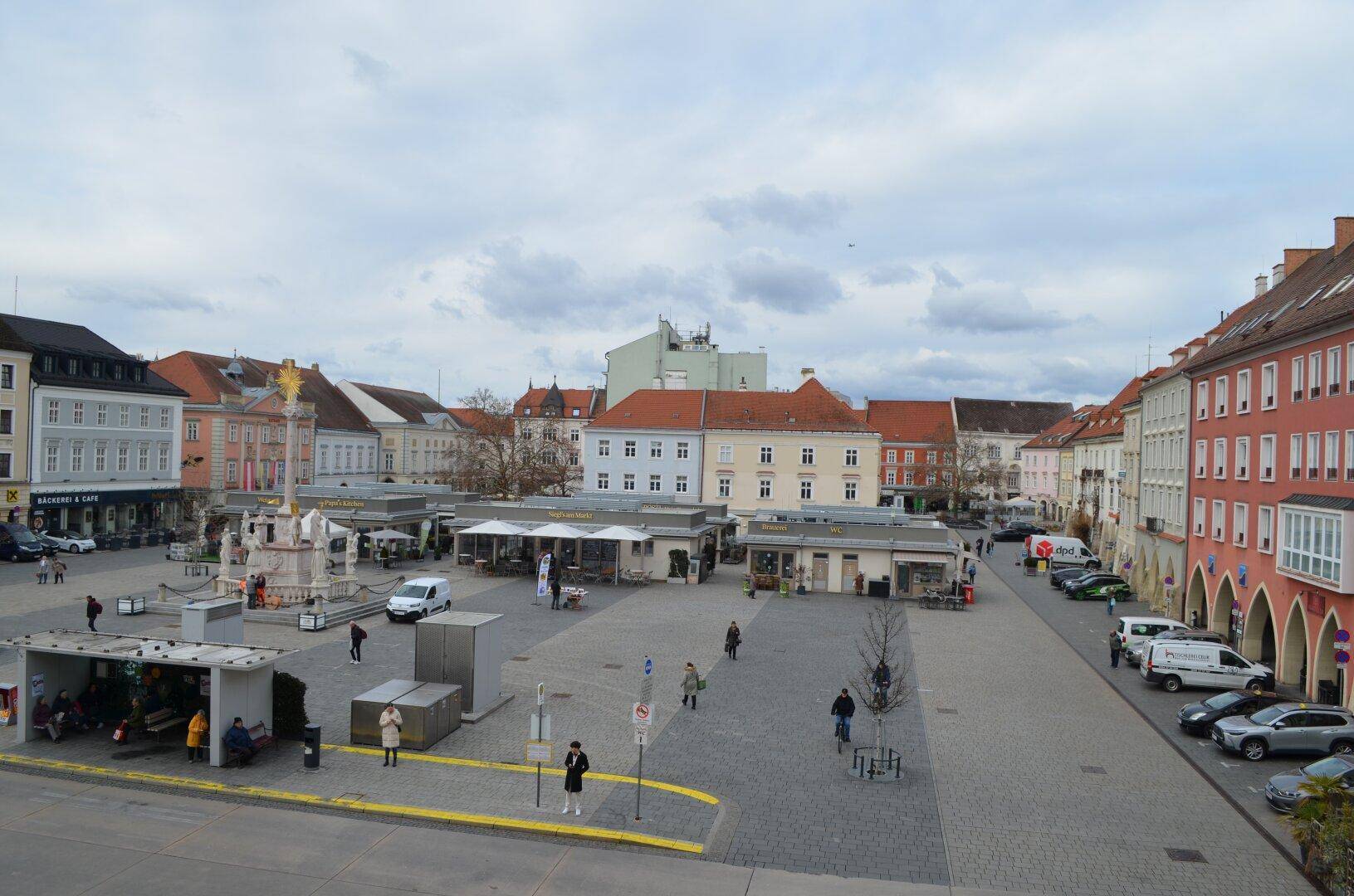 Weitläufiger Stadtplatz mit historischen Gebäuden und belebter Atmosphäre.
