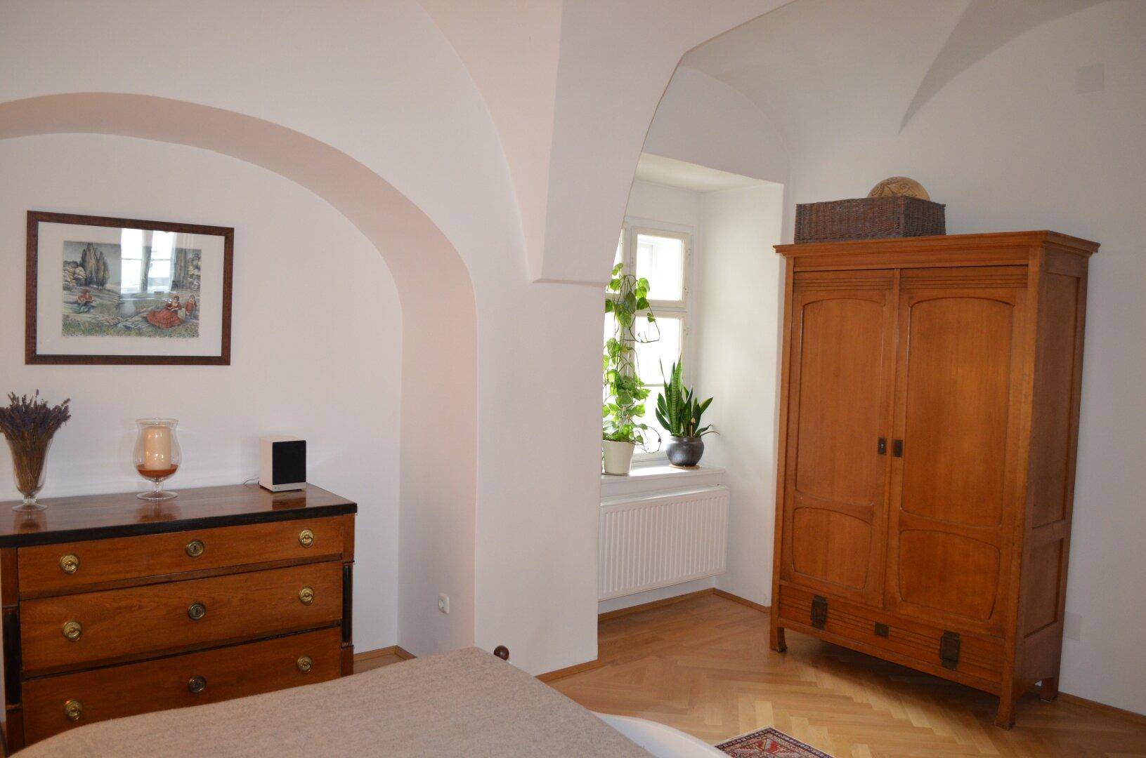 Schlafzimmer mit Gewölbedecke, Holzboden und einem Fenster mit Blick ins Grüne.