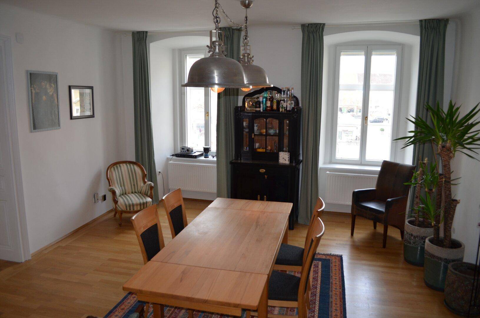 Klassischer Essbereich mit Holztisch, Teppich und einem dunklen Schrank zwischen den Fenstern.
