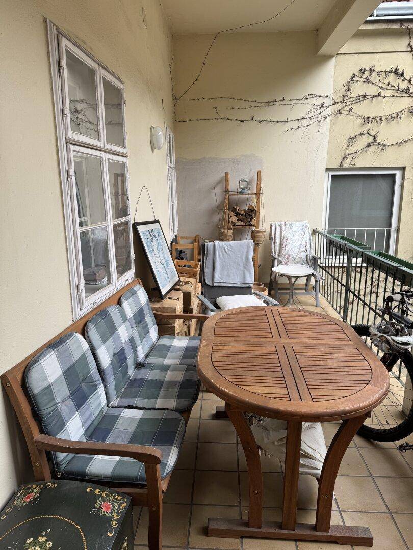 Gemütlicher Balkon mit Holztisch, Sitzbank und Fliesenboden.