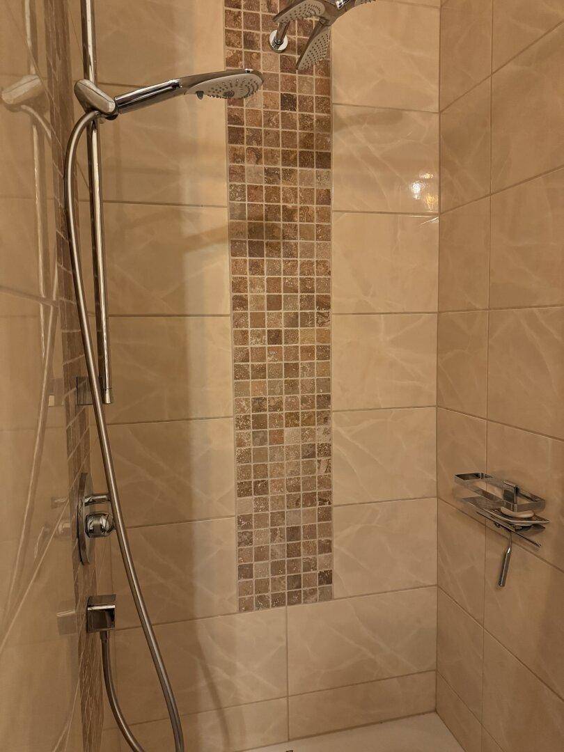 Duschbereich mit beigen Fliesen und einer dekorativen Mosaikbordüre.