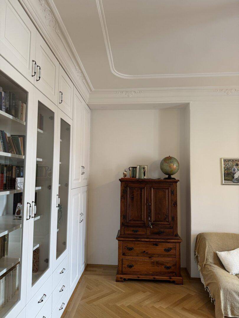 Detailansicht der hohen Decke mit Stuckverzierung und einem antiken Holzschrank.