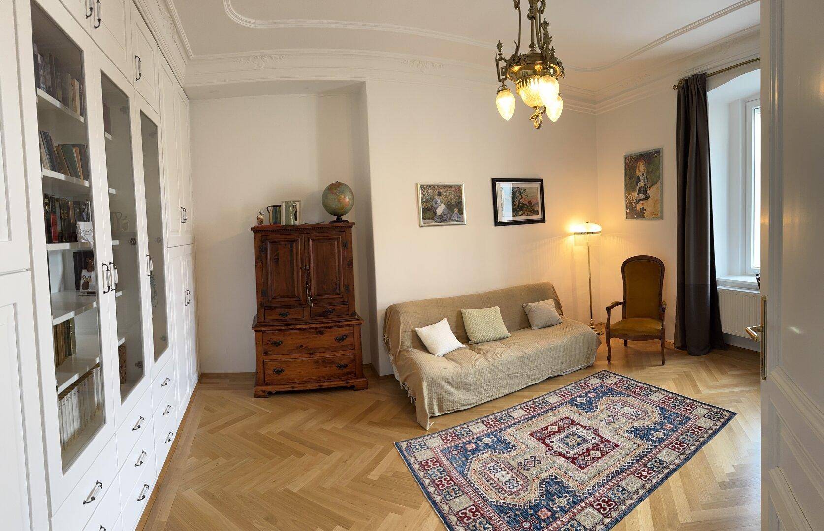 Elegantes Wohnzimmer mit Fischgrätparkett, großen Bücherregalen und einem Sofa.