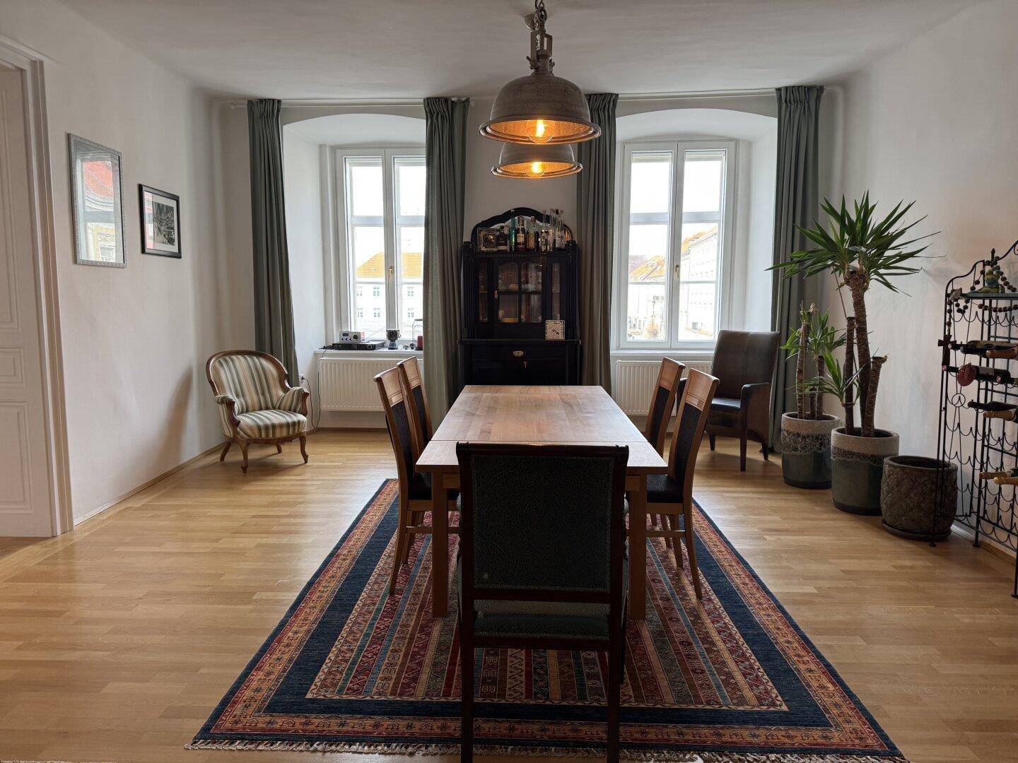 Geräumiger Essbereich mit Holztisch, Teppich und zwei großen Fenstern, die viel Tageslicht hereinlassen.