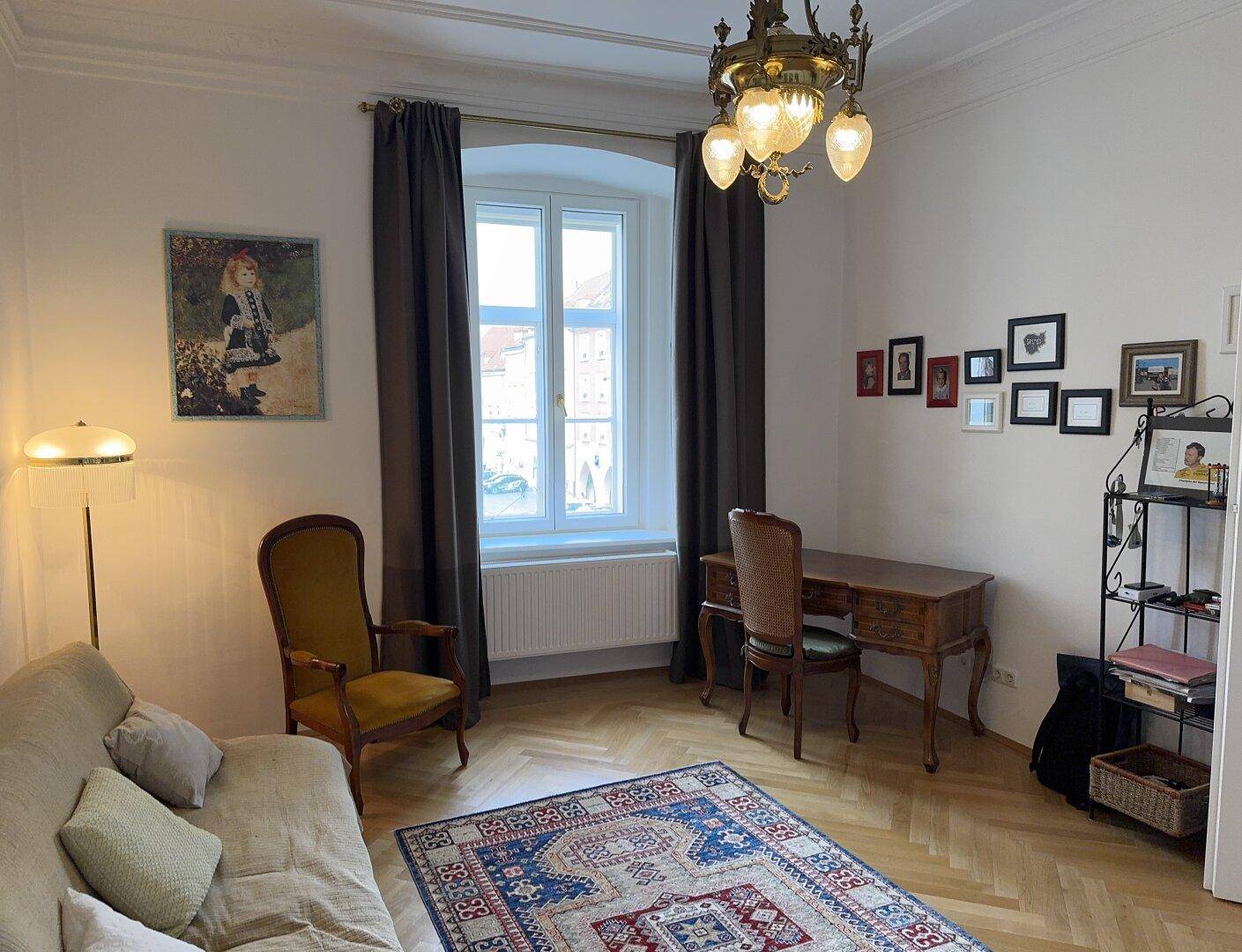 Helles Wohnzimmer mit Fischgrätparkett, Schreibtisch und einem eleganten Kronleuchter.