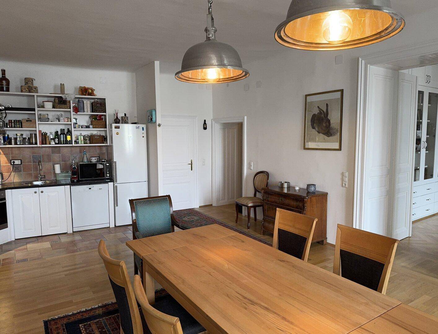 Offener Wohn- und Essbereich mit Holztisch und Blick auf eine angrenzende Küchenzeile.
