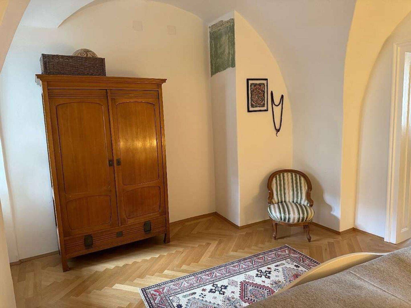 Schlafzimmer mit Gewölbedecke, Holzboden und einem antiken Kleiderschrank.