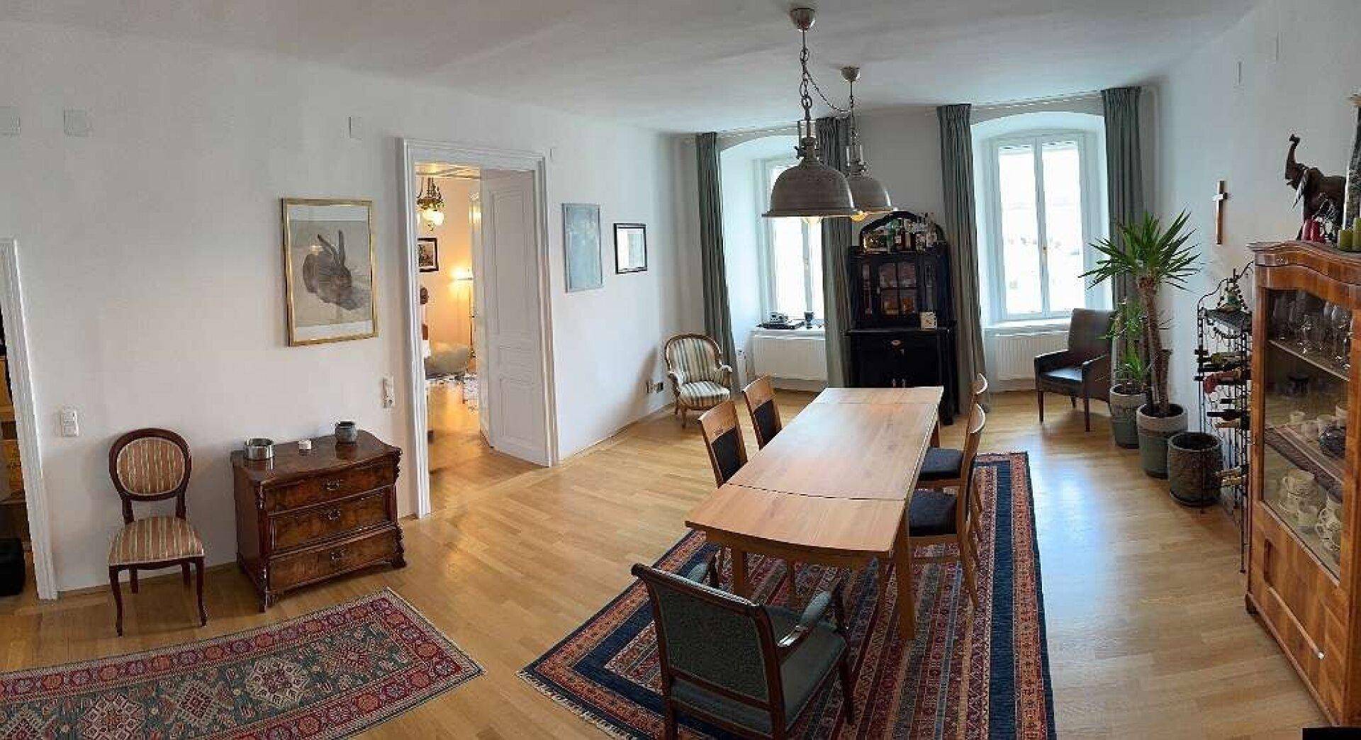 Geräumiger Wohn-Essbereich mit Holzboden, Teppichen und Zugang zu einem weiteren Zimmer.