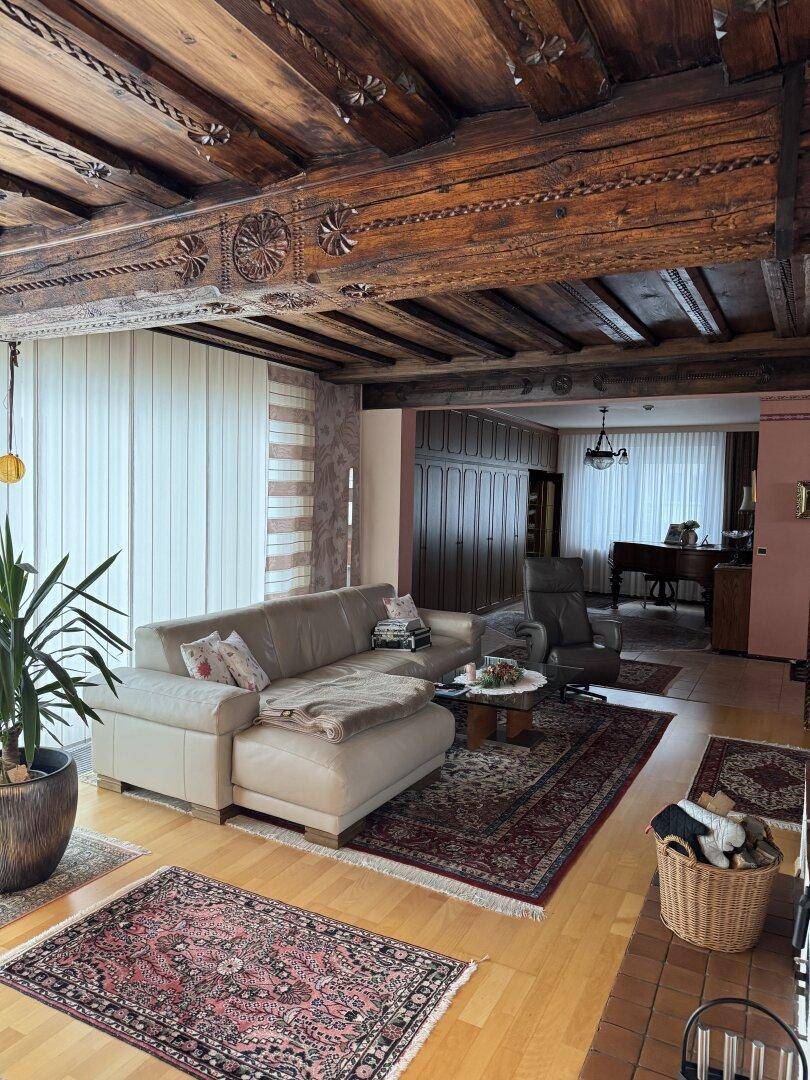 Geräumiger Wohnbereich mit beeindruckender Holzbalkendecke, Ledersofa und traditionellen Teppichen.