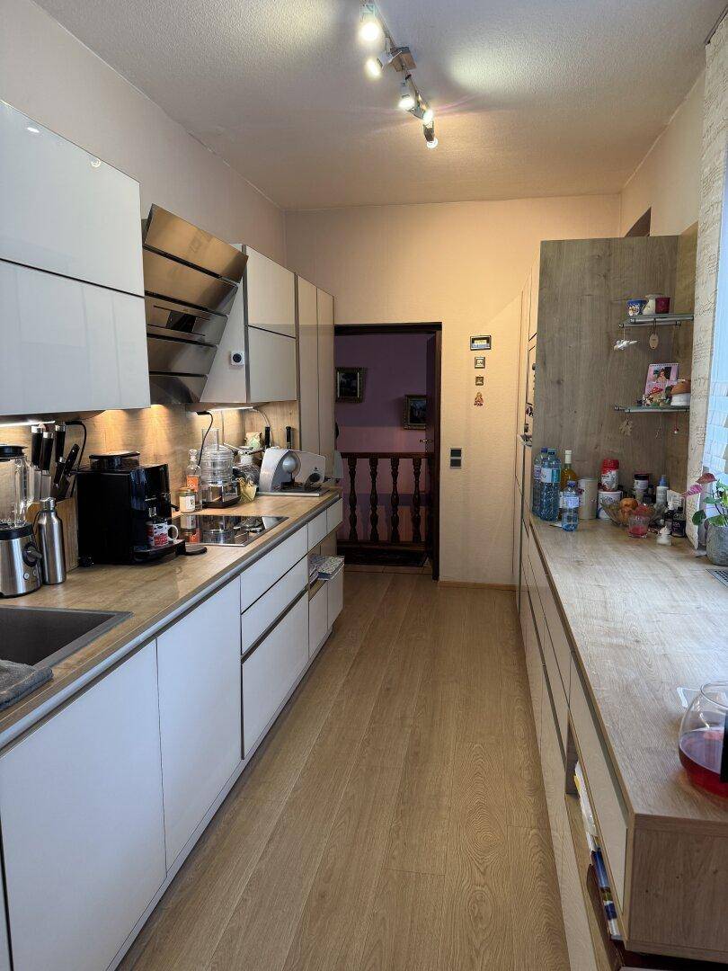 Moderne Küche mit weißen Hochglanzfronten, Holzarbeitsplatten und integrierten Geräten.