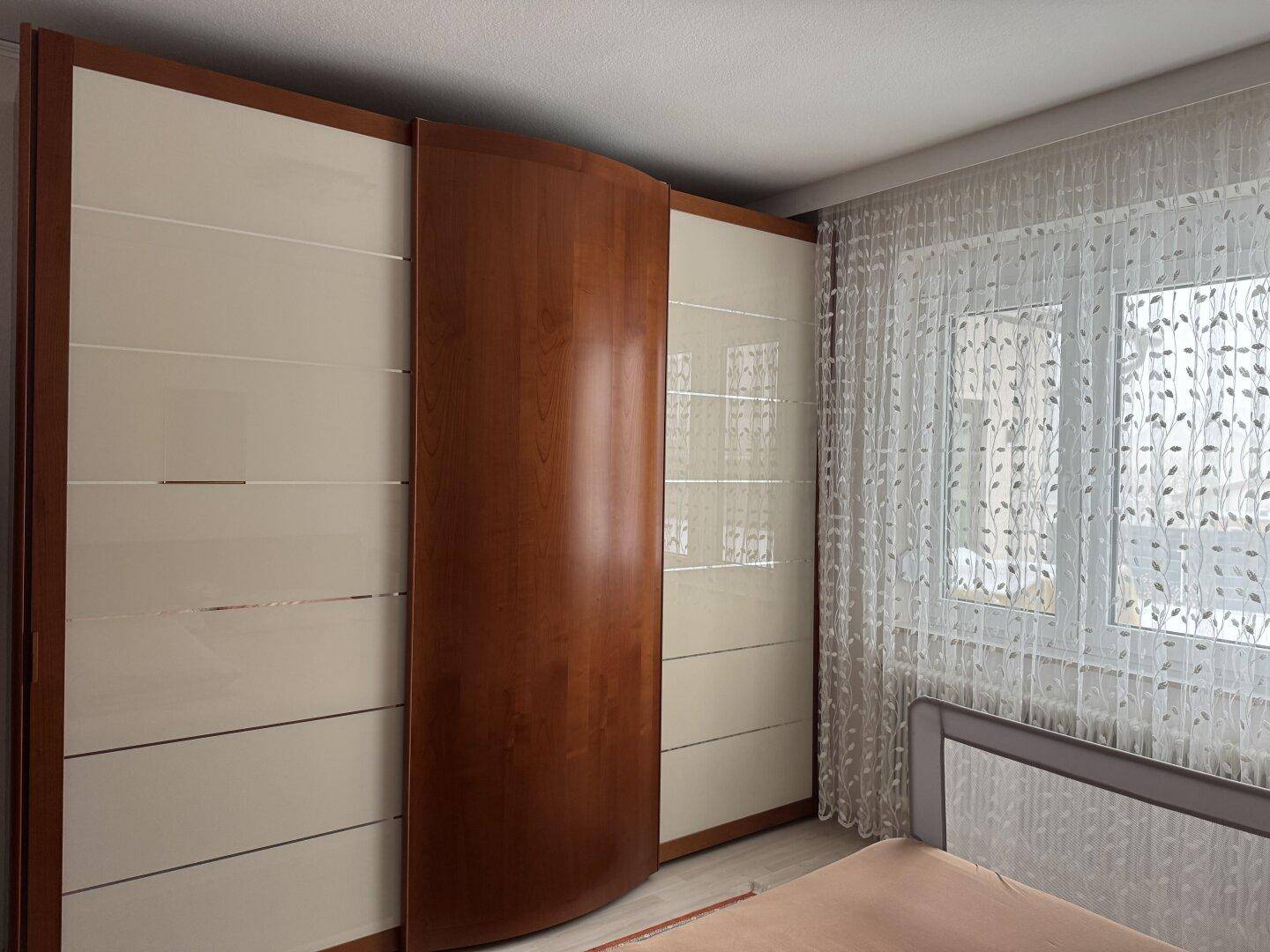 Schlafzimmer mit großem Einbauschrank, hellen Vorhängen und viel Tageslicht.