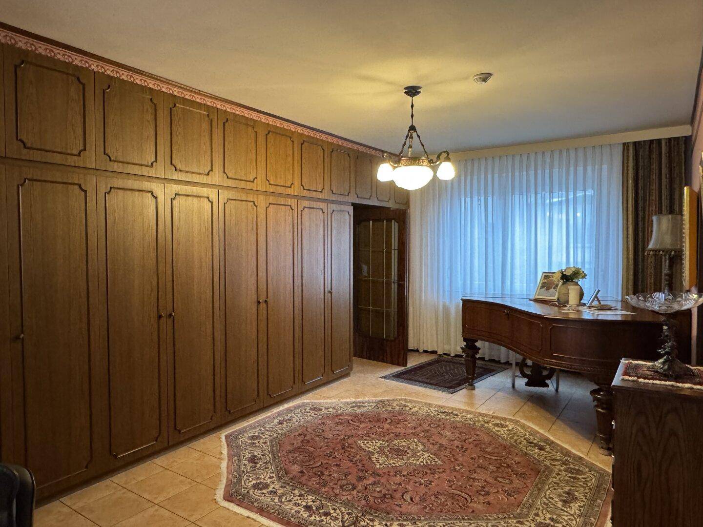 Elegantes Zimmer mit großem Flügel, Einbauschränken und traditionellem Teppichboden.
