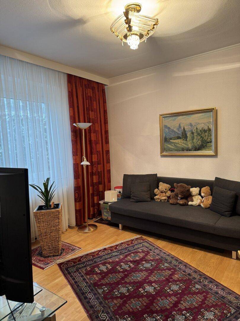 Gemütliches Wohnzimmer mit Sofa, Fernseher und großen Fenstern mit roten Vorhängen.