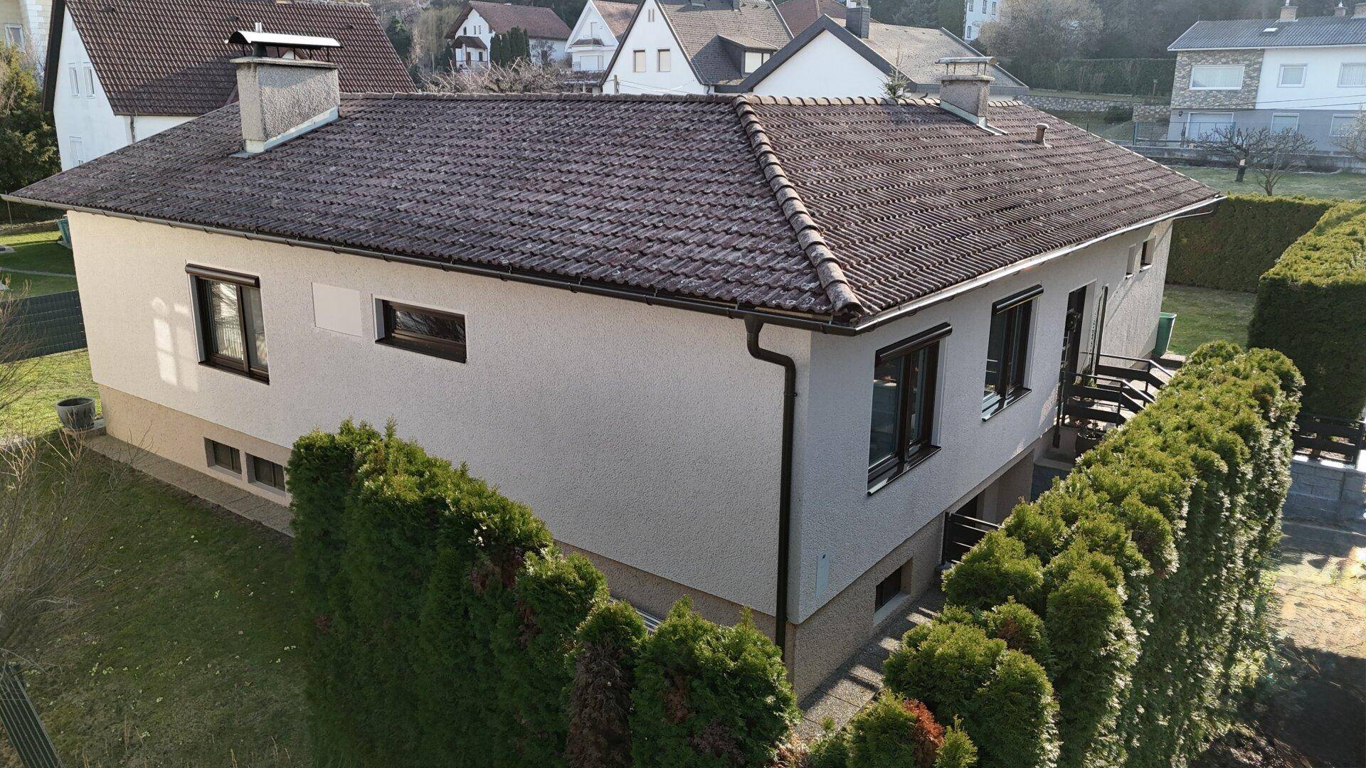 Luftaufnahme des Hauses von der Seite mit Dach, Fenstern und umliegender Hecke.