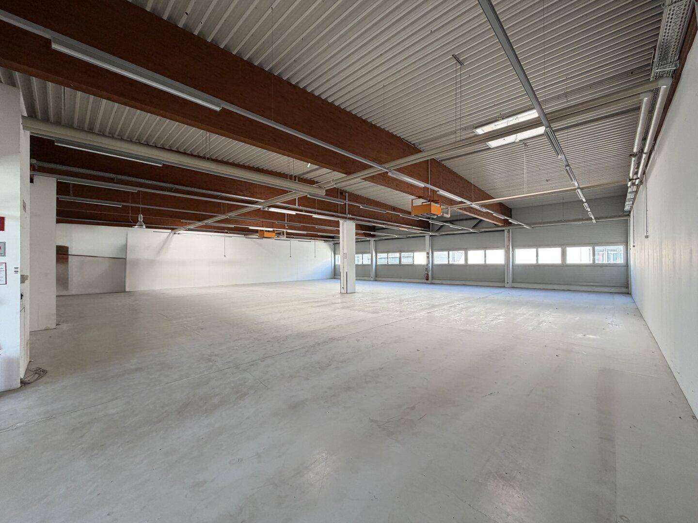 Großer, leerer Gewerberaum mit hoher Decke, sichtbaren Holzbalken und Betonboden.
