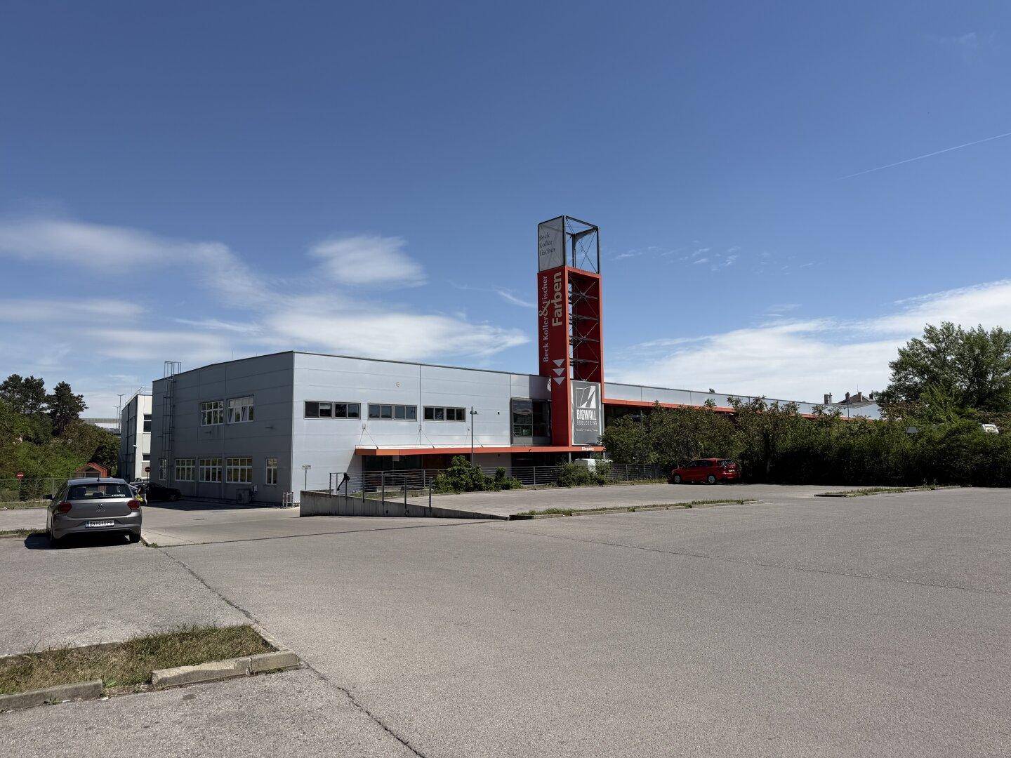 Weitwinkelansicht des Geschäftsgebäudes von der Rückseite mit großem Parkplatz und umliegender Vegetation.