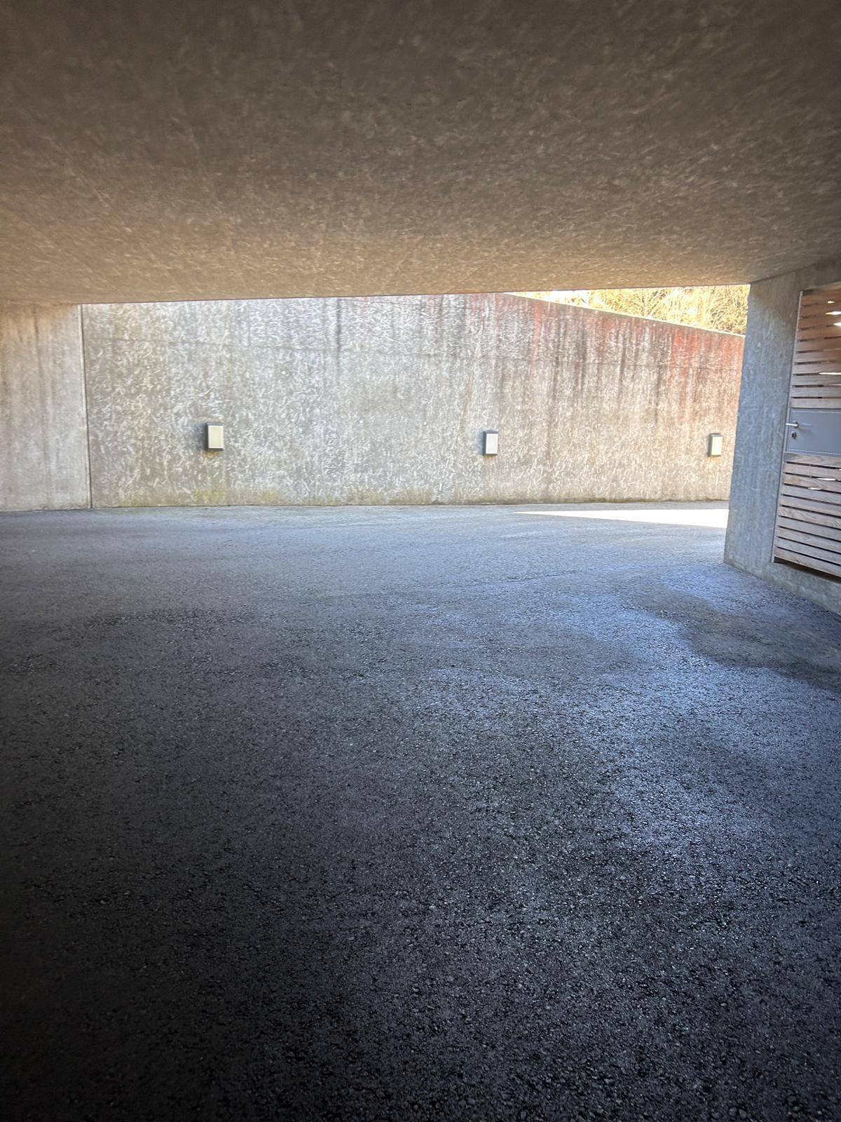 Überdachter Parkbereich mit Betonwänden und Asphaltboden, der Tageslicht von der Seite erhält.