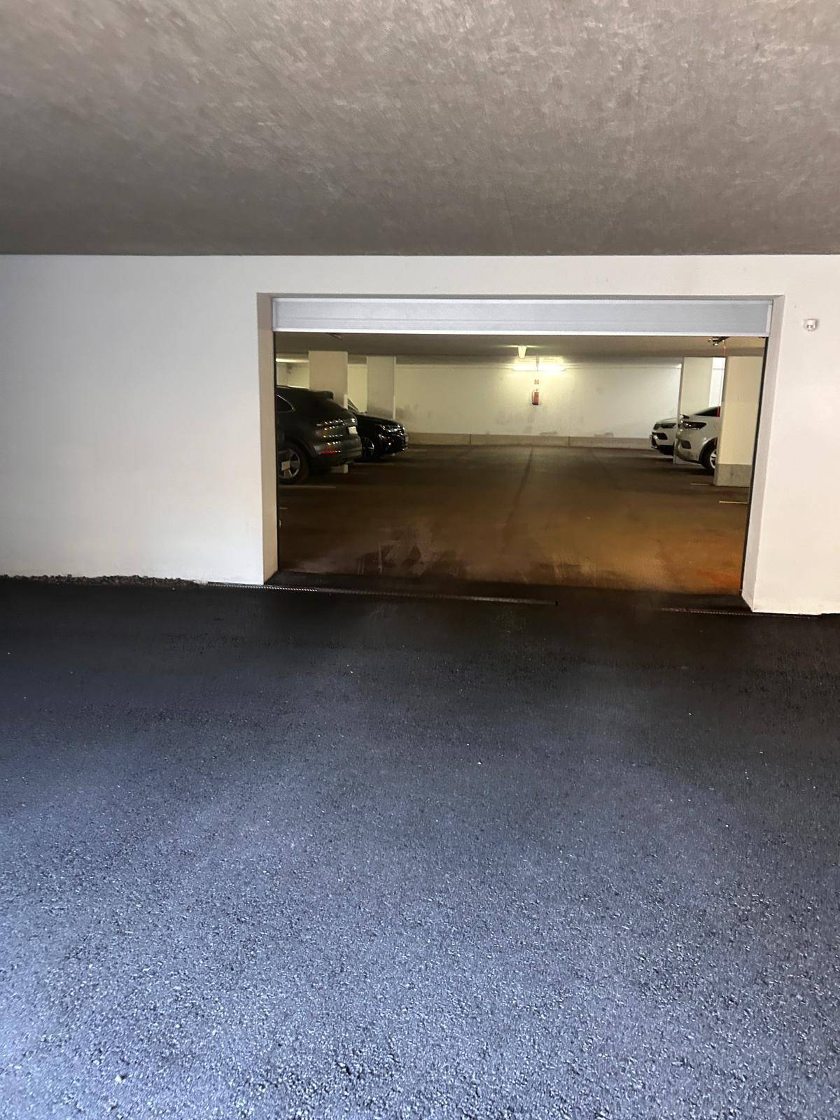 Eingang zu einer Tiefgarage mit mehreren geparkten Fahrzeugen und Asphaltboden.