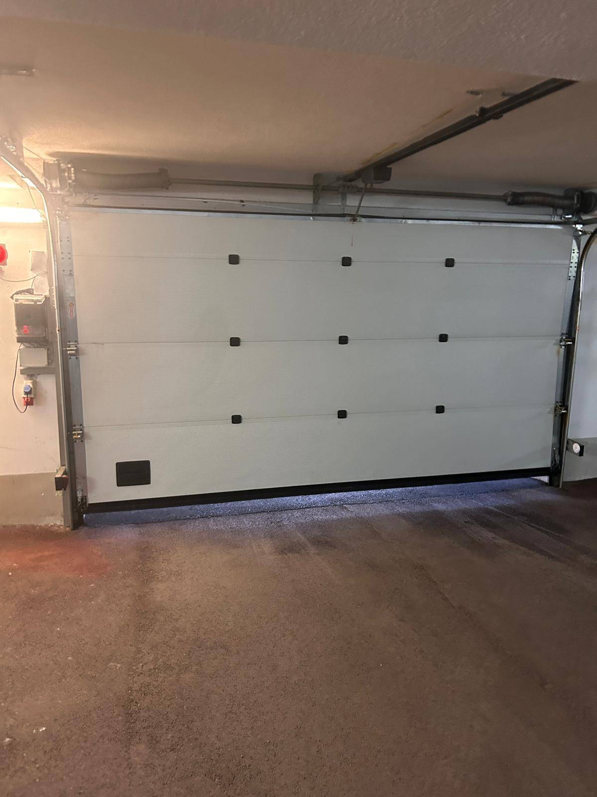 Eine weiße Garagentür in einer Tiefgarage, die sich öffnet und den Innenraum beleuchtet.