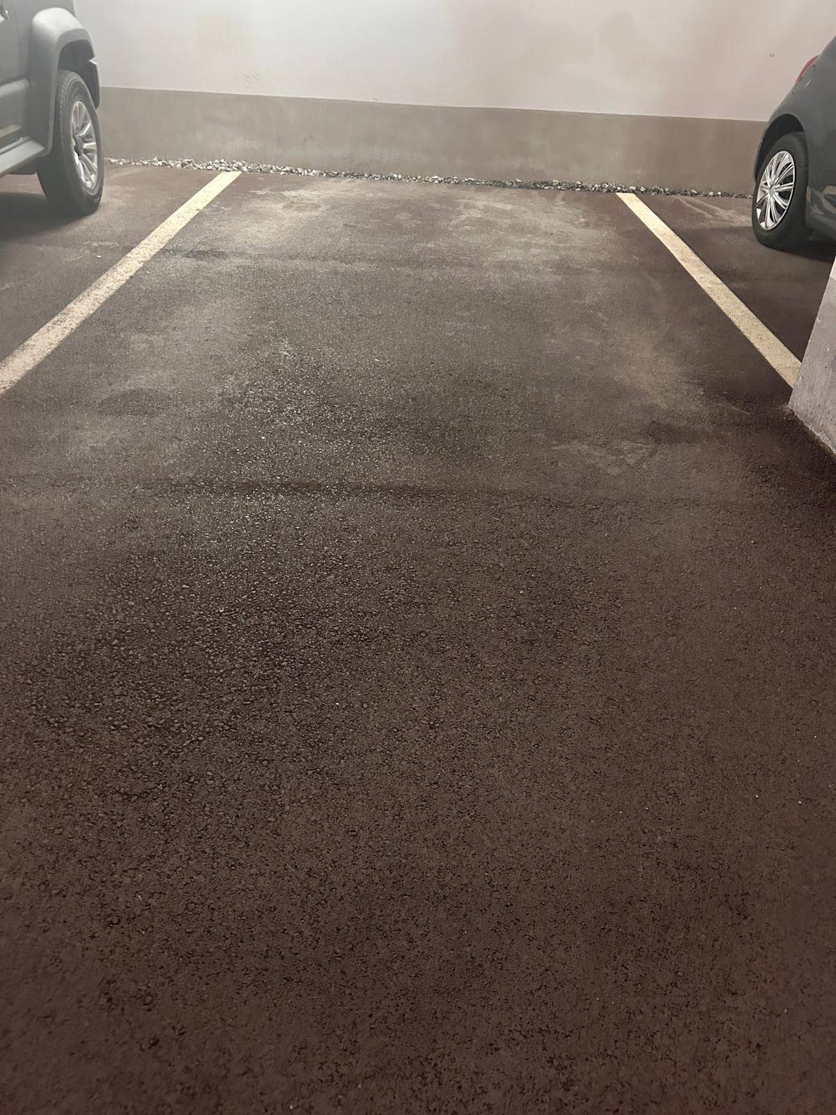 Ein leerer Parkplatz in einer Tiefgarage, markiert mit weißen Linien auf dunklem Asphaltboden.