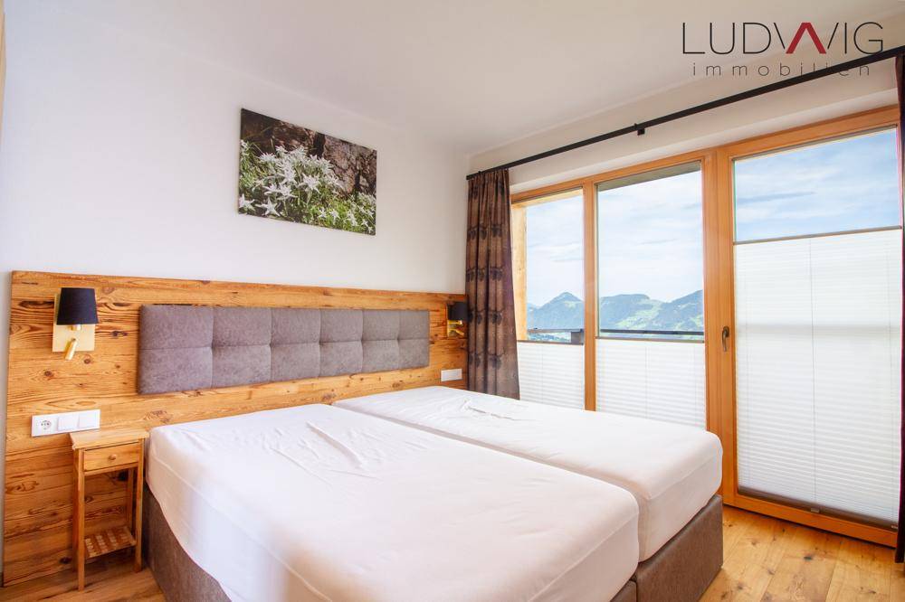 Helles Schlafzimmer mit zwei Einzelbetten, Holzkopfteil und Balkonzugang mit Bergblick.