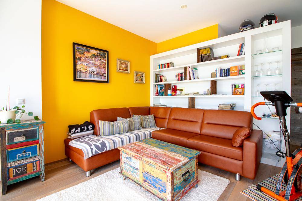 Detailansicht des Wohnzimmers mit Ledersofa, bunter Truhe und gelber Wand.