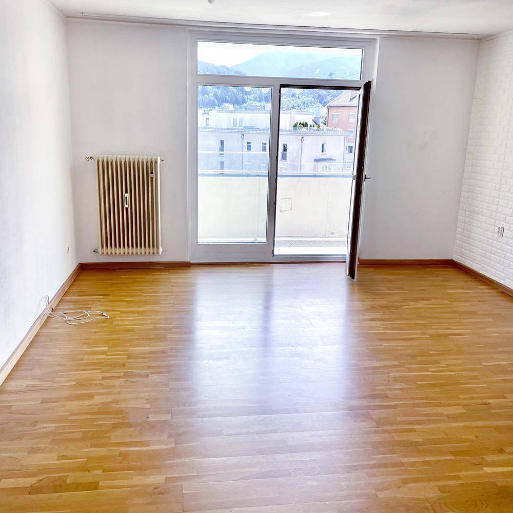 Heller Raum mit Holzboden, Balkonzugang und Bergblick.