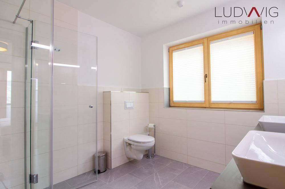 Modernes Badezimmer mit begehbarer Dusche, wandhängendem WC und zwei Waschbecken.
