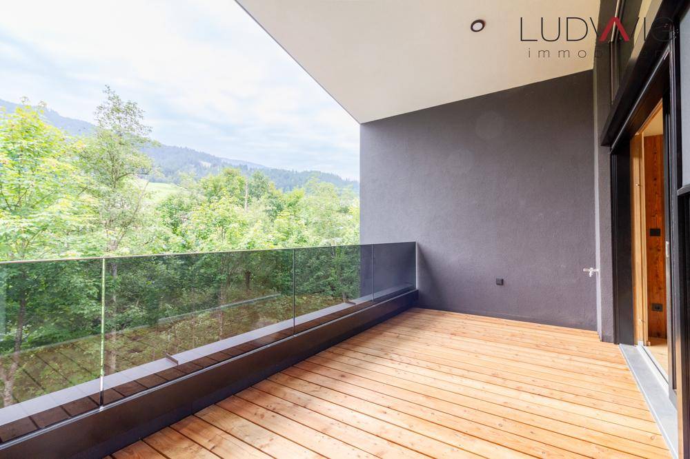 Moderner Balkon mit Holzbelag und Glasgeländer, bietet einen weiten Blick auf die Berge.