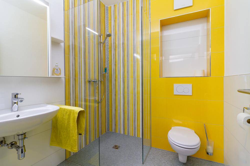 Farbenfrohes Badezimmer mit gelben Fliesen, Dusche und wandhängendem WC.
