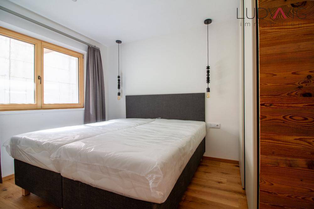 Helles Schlafzimmer mit Holzboden, großem Fenster und schlichter, moderner Einrichtung.