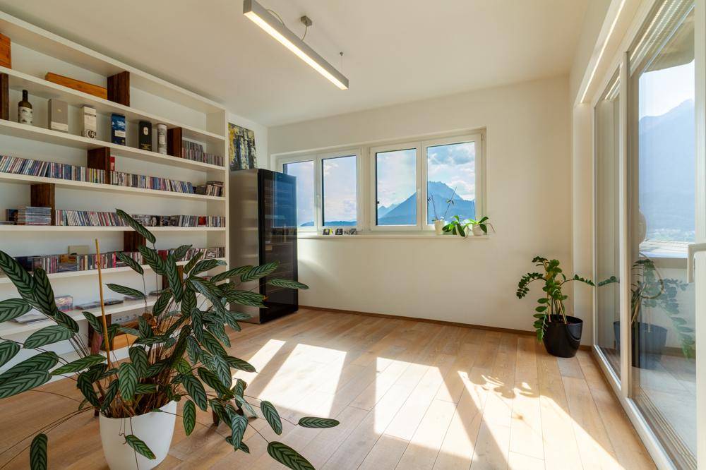 Heller Raum mit Holzboden, Bücherregal und weitem Bergblick durch große Fenster.