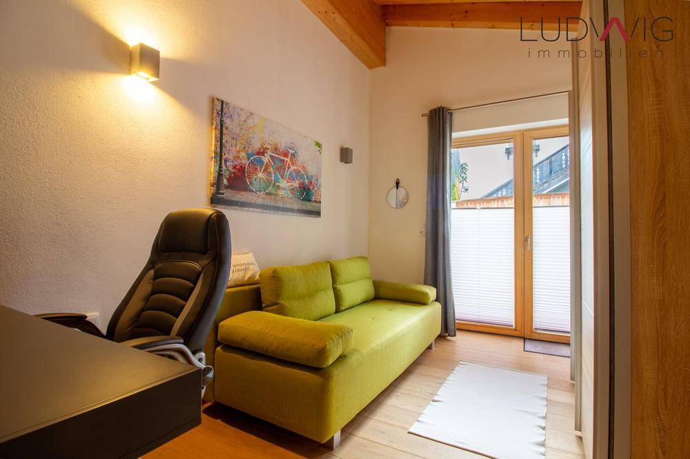Helles Zimmer mit Schlafsofa, Schreibtisch und Zugang zu einem kleinen Balkon.