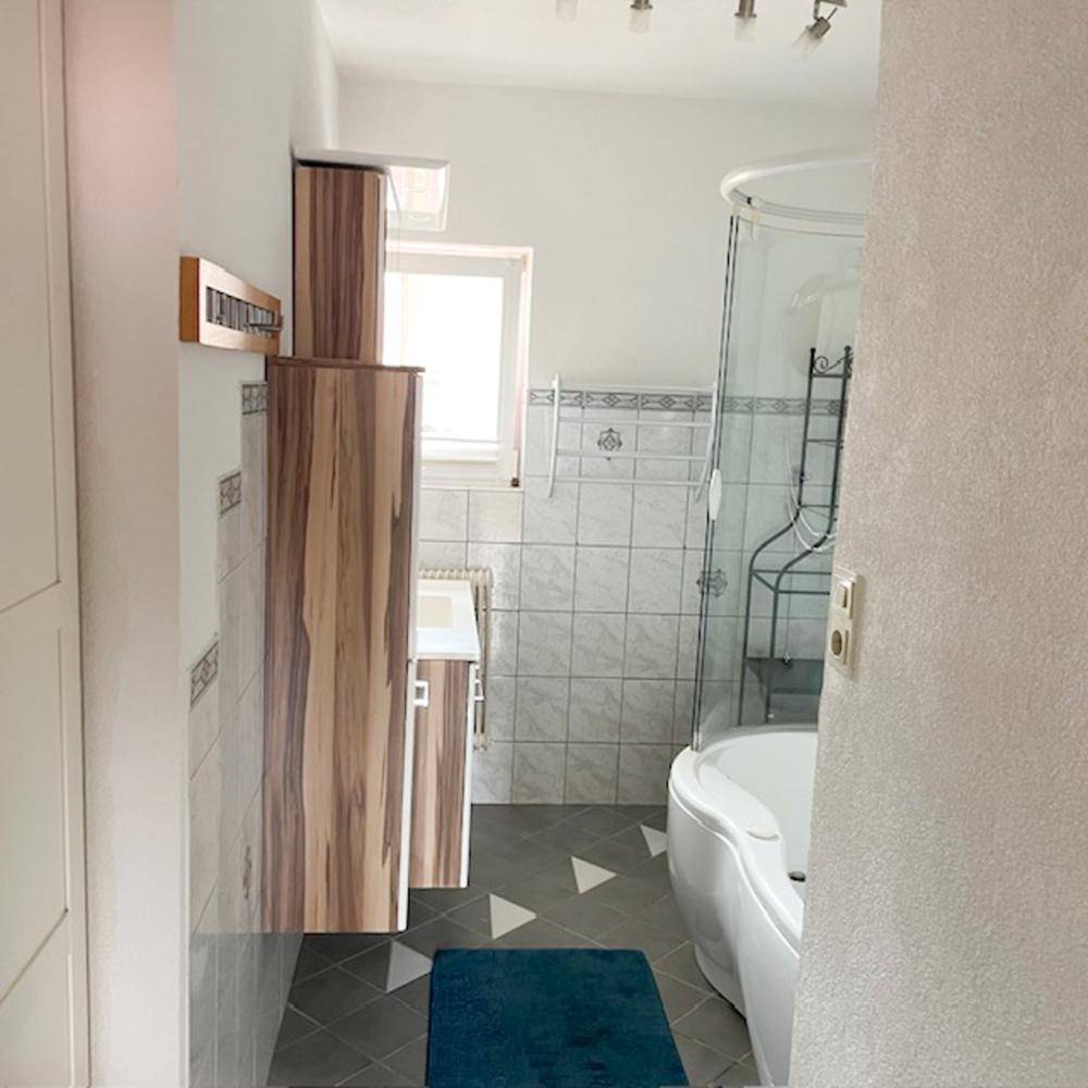 Badezimmer mit Duschkabine, Badewanne, Fenster und Holzschränken.