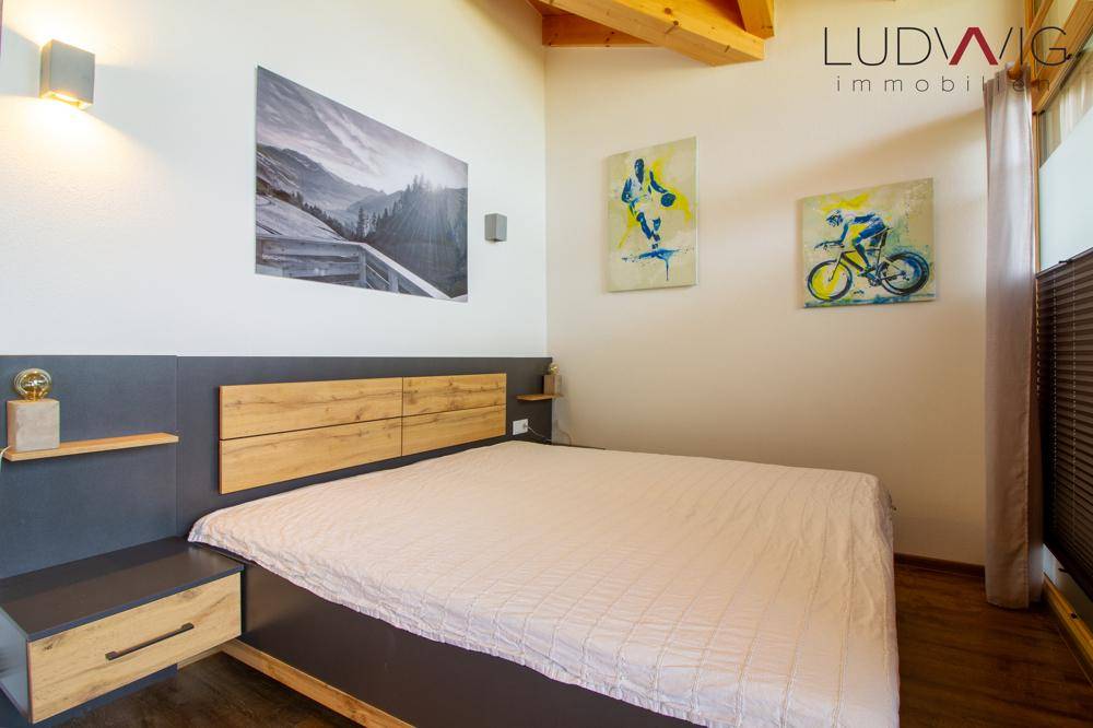 Modernes Schlafzimmer mit Doppelbett, Holzkopfteil und dekorativen Wandbildern.
