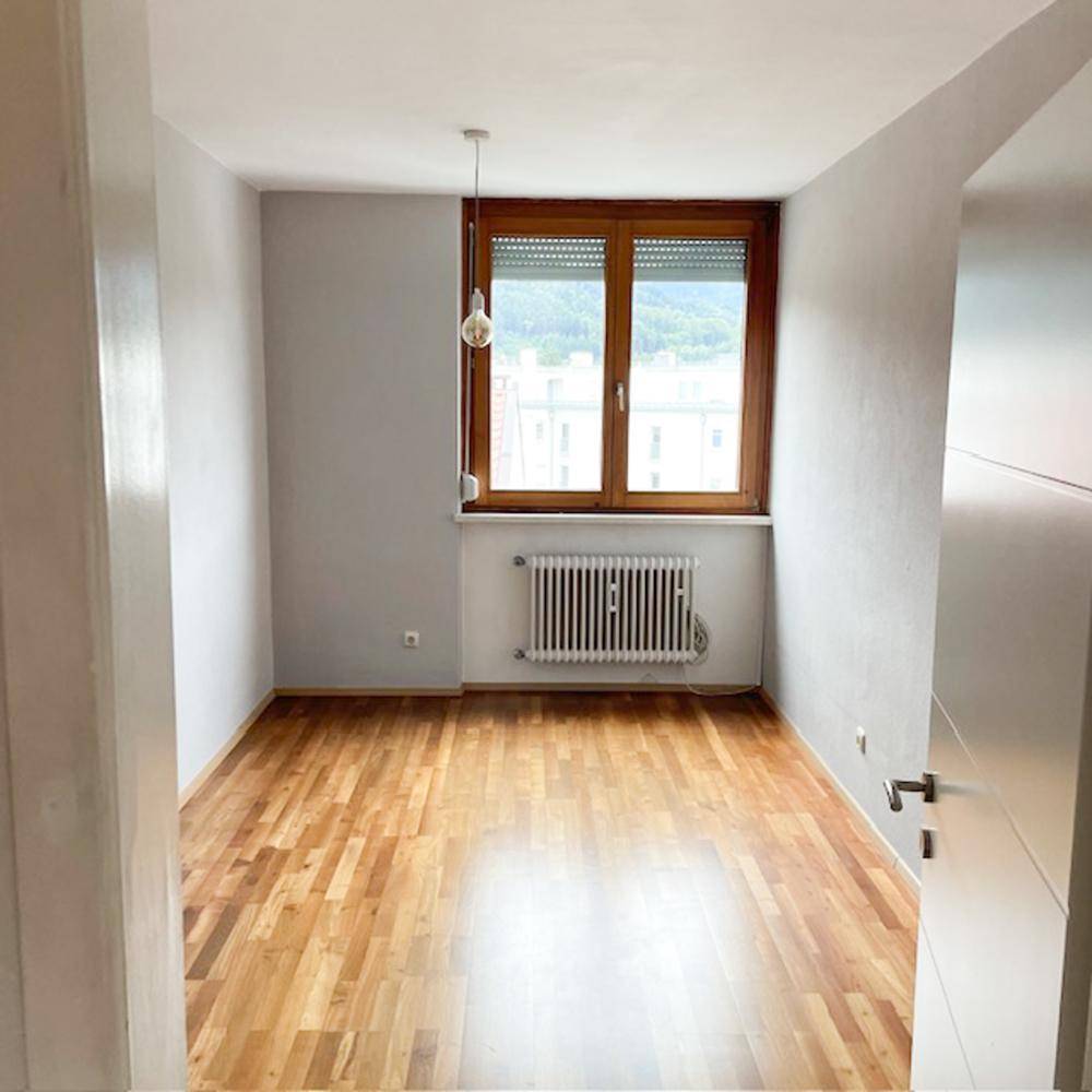 Leerer Raum mit Holzboden, großem Fenster und Heizkörper.