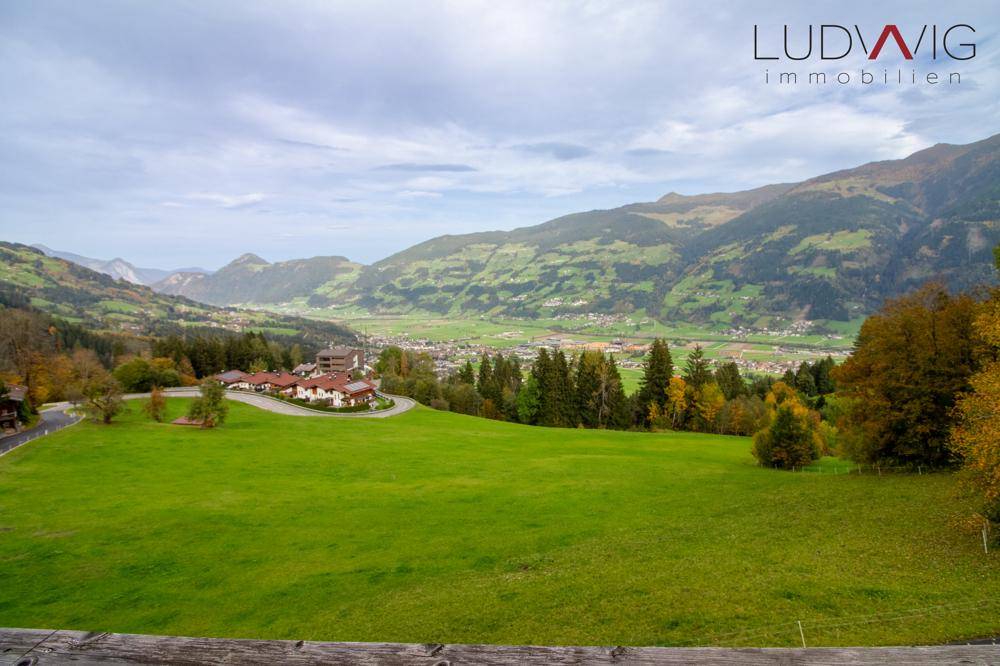 Weitläufiger Blick über eine grüne Wiese und das malerische Tal mit umliegenden Bergen.