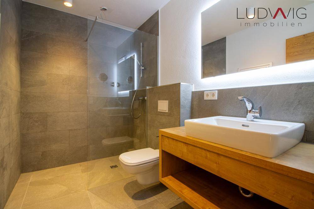 Elegantes Badezimmer mit begehbarer Dusche, modernem Waschtisch und beleuchtetem Spiegel.