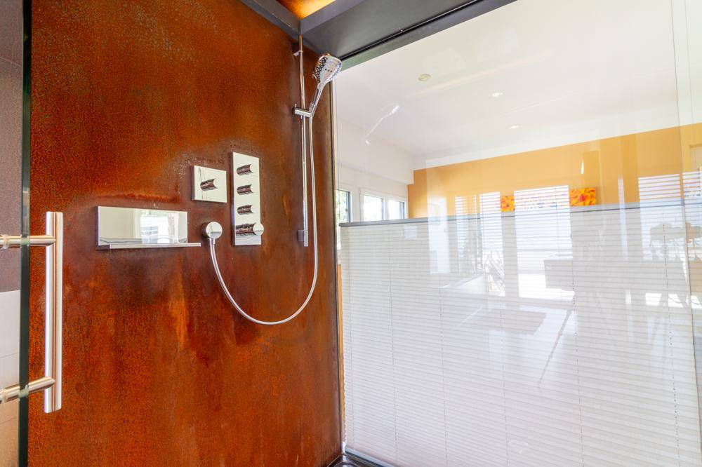 Moderne begehbare Dusche mit rostfarbener Wandverkleidung und Regenduschkopf.
