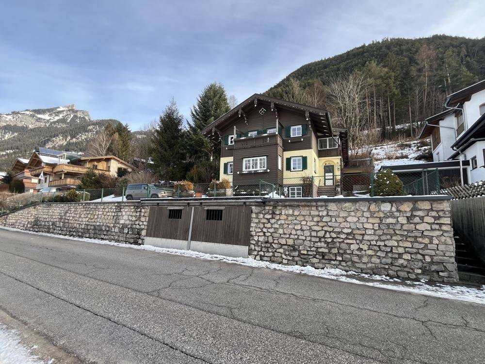 Alpines Wohnhaus mit Steinfassade, integrierter Garage und verschneiter Umgebung.