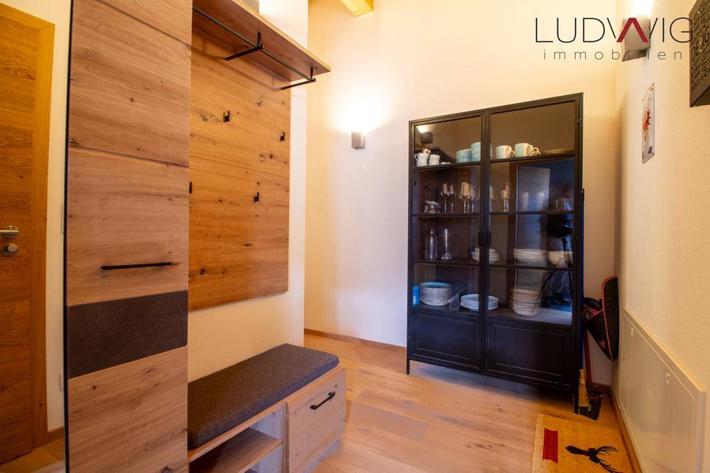Heller Eingangsbereich mit Holzboden, Garderobe und einem Vitrinenschrank.