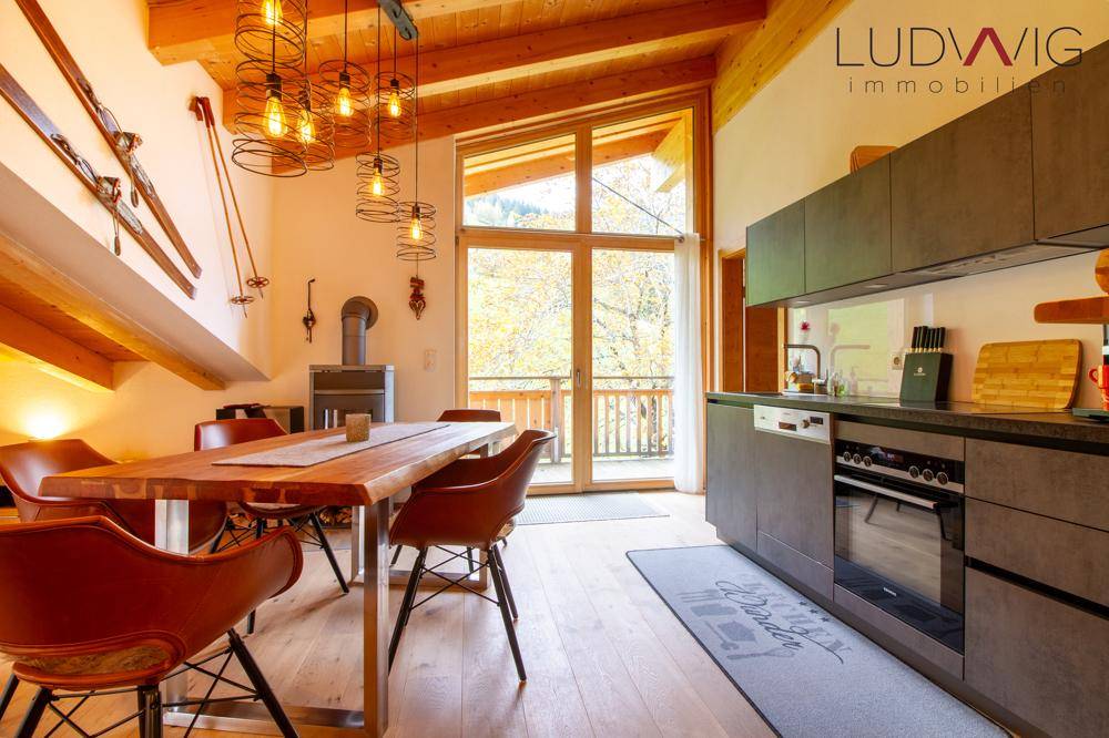 Moderne Küche mit Essbereich, Kaminofen und großen Fenstern mit Blick ins Grüne.